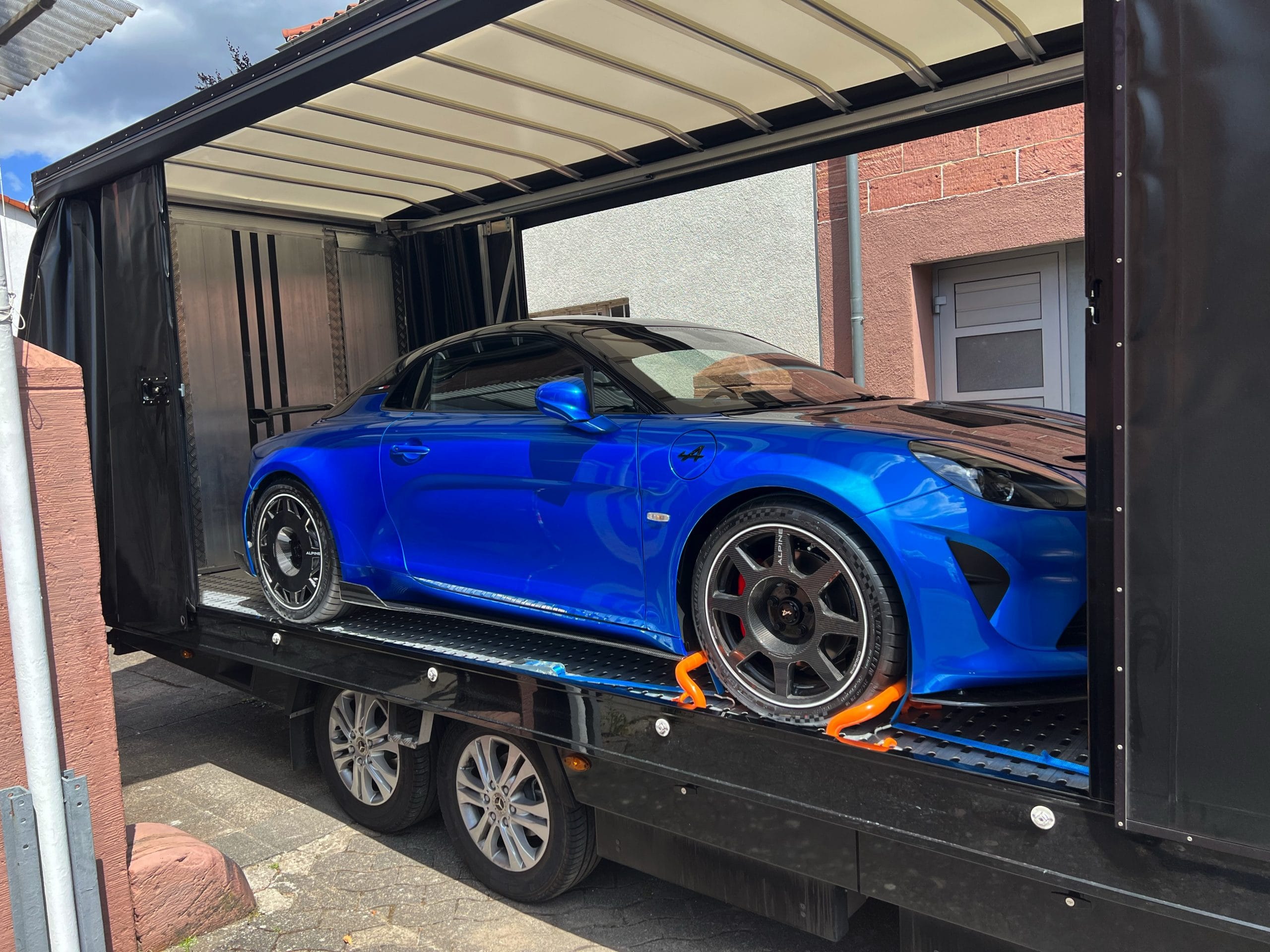 Blauer Alpine Sportwagen gesichert im geschlossenen Fahrzeuganhänger